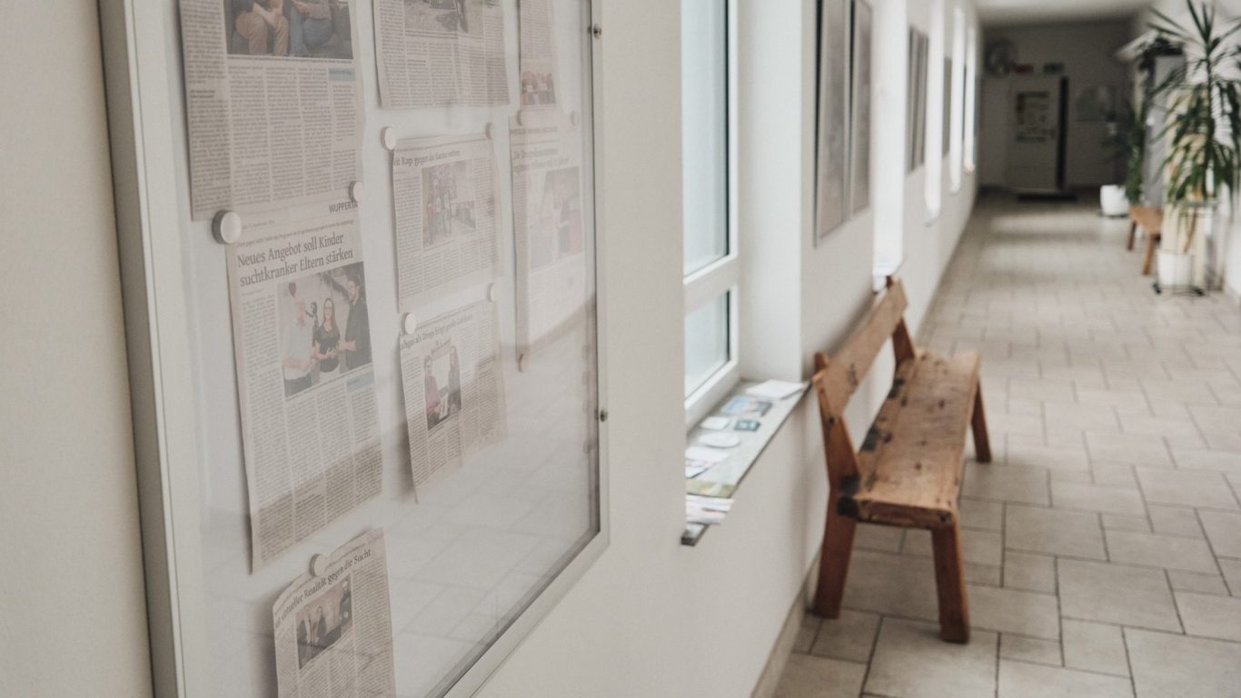 Ein heller Flur mit Wandzeitungen und einer Holzbank im Vordergrund.