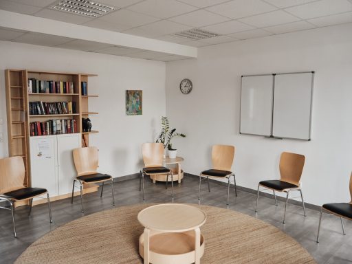 Leerer Besprechungsraum mit Stühlen, Tisch, Bücherregal und Wandtafel.