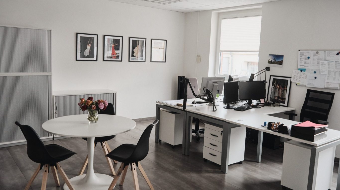 Helles Büro mit Schreibtischen, Computern und einem runden Tisch mit Blumen.